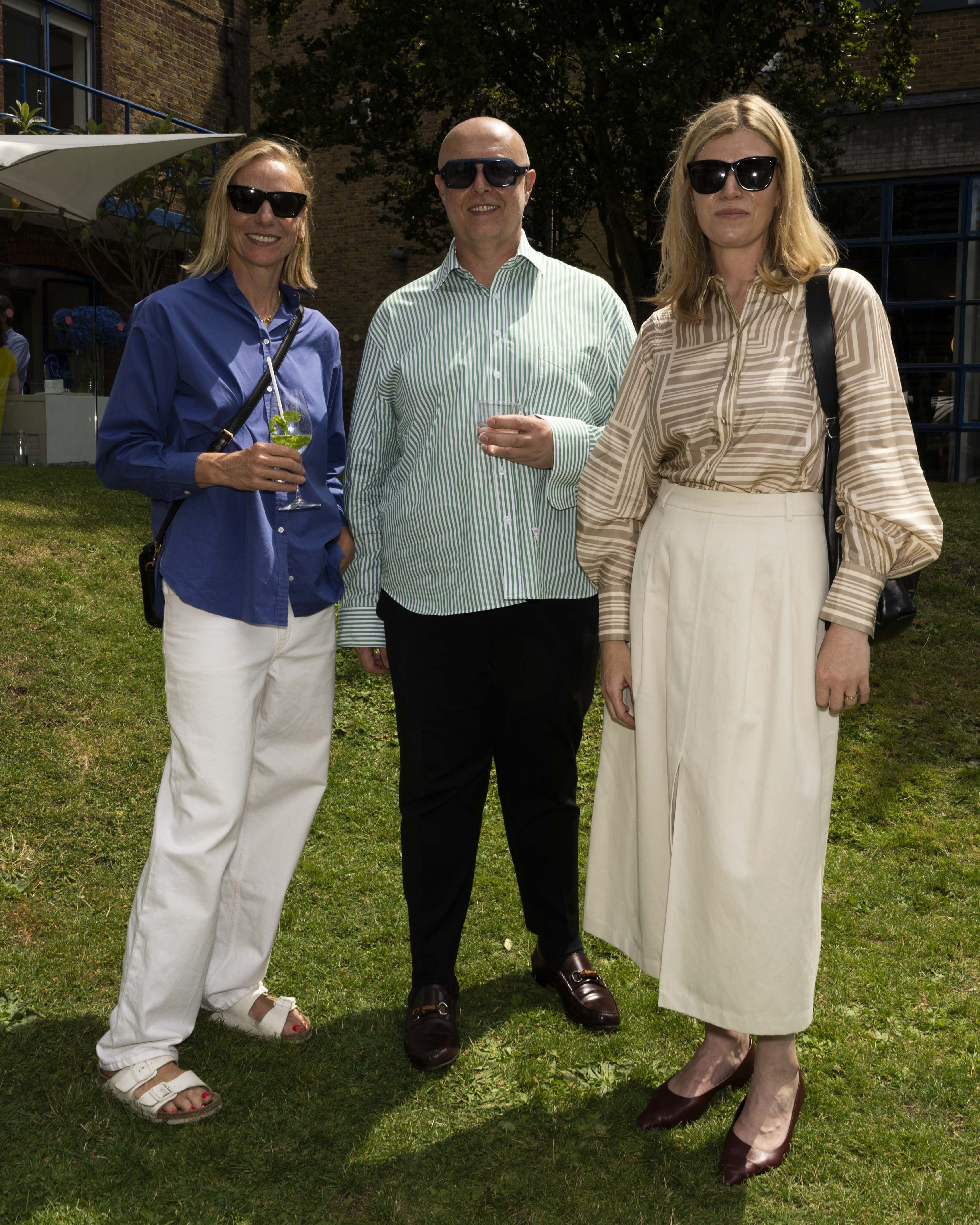 Cathy Kasterine, Mario Arena, Laura Atkinson at a summer event wearing sunglasses, with the woman on the left in a blue shirt and white pants, the man in the center wearing a light green striped shirt and black trousers, and the woman on the right in a beige striped blouse and white skirt.