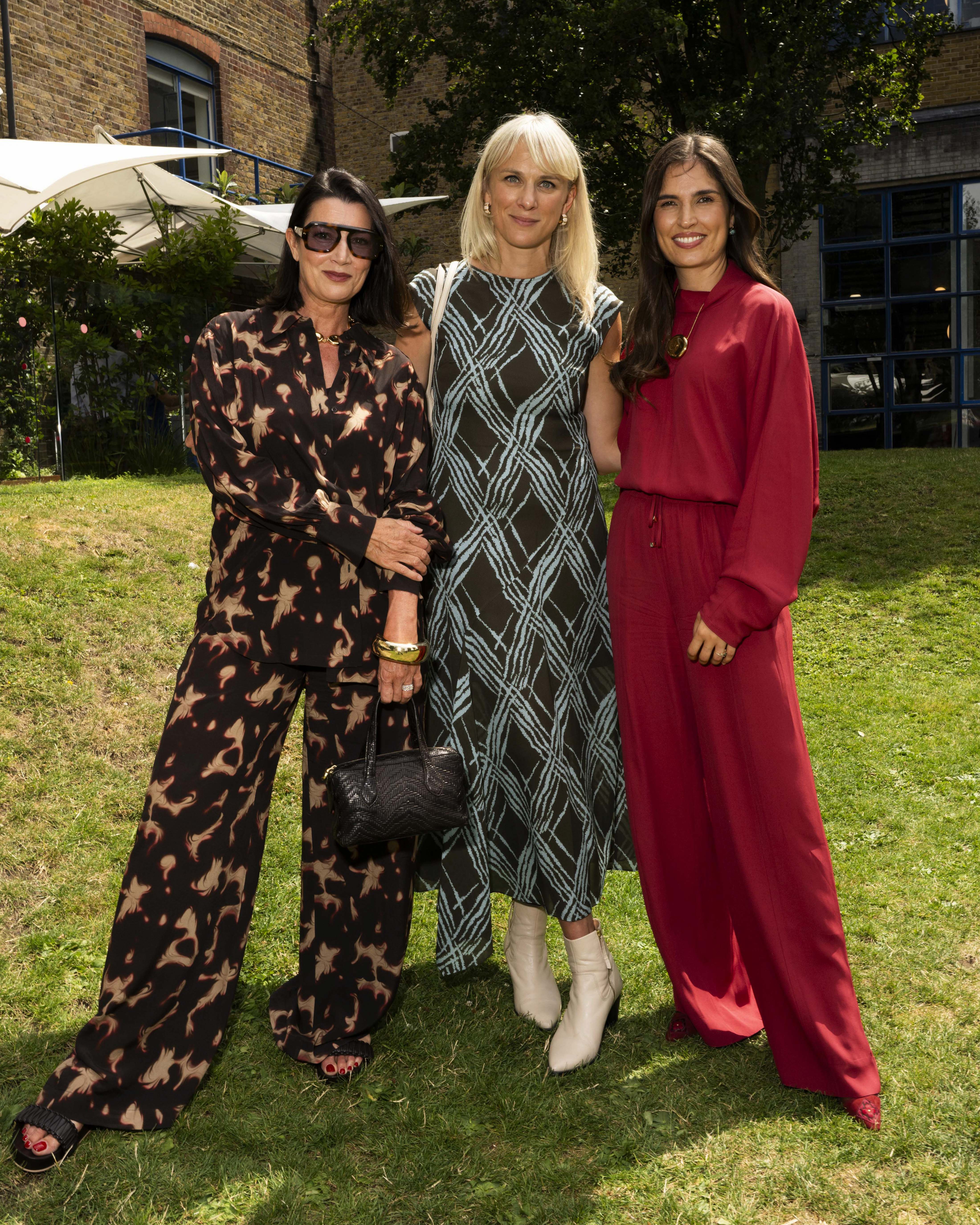 Barbara Campos, Kirsty McGregor, Marine Tanguy posing together at a summer event. The woman on the left wears a brown and black animal print wide-leg jumpsuit, the middle woman wears a black and teal geometric patterned dress, and the woman on the right wears a solid red wide-leg co-ord.